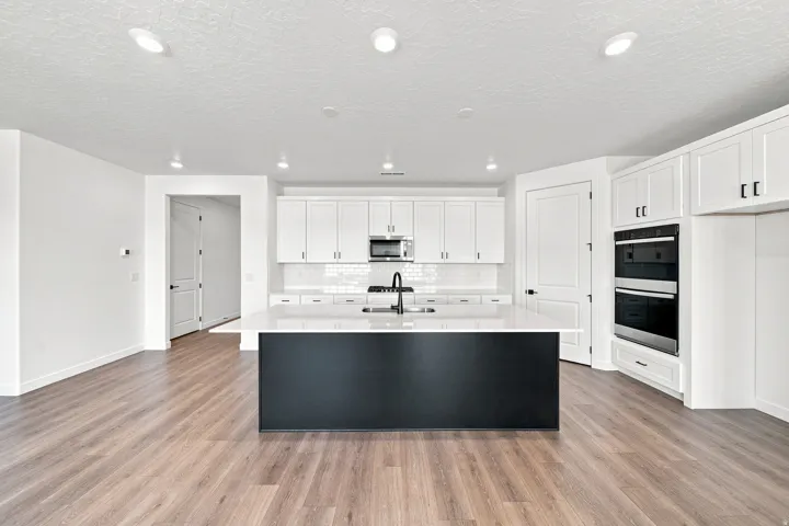 Kitchen featuring a large central island with a sink, white cabinetry, integrated double ovens, and wood-finish flooring