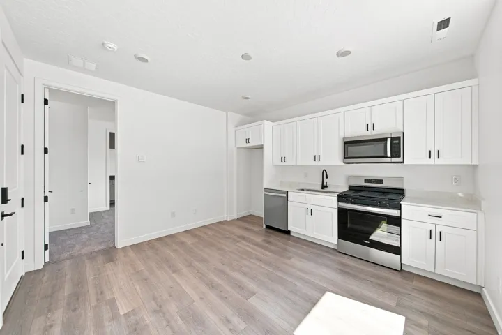 Kitchen featuring wood-finish flooring, white cabinetry, stainless steel appliances, and a black faucet