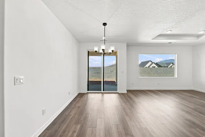 Open-concept living area featuring wood-finish flooring, a contemporary chandelier, a sliding glass door, and a large window with mountain scenery