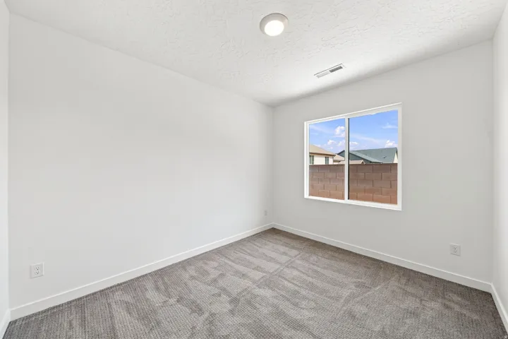 White walls, textured ceiling, contemporary flush mount light fixture, large window, and patterned carpet flooring