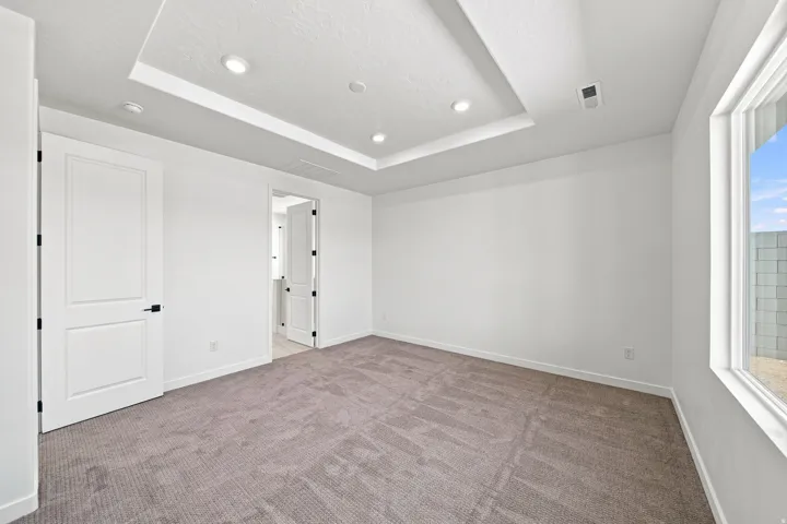 Recessed lighting illuminates the tray ceiling, complementing the neutral-toned carpet and white walls