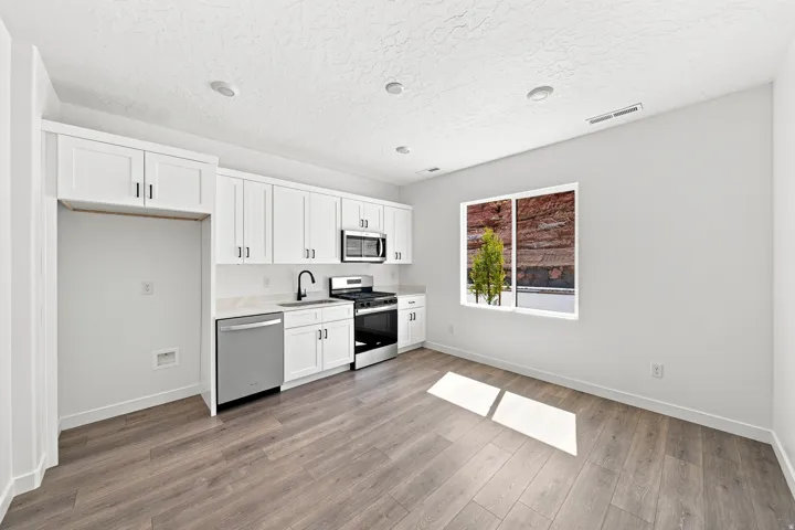 Modern kitchen area featuring white shaker cabinetry, stainless steel appliances, a black matte faucet, and wood-finish flooring