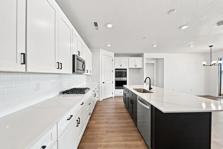 Kitchen featuring white cabinetry, a gas range, white subway tile backsplash, a center island with a stainless steel sink, and wood-finish flooring