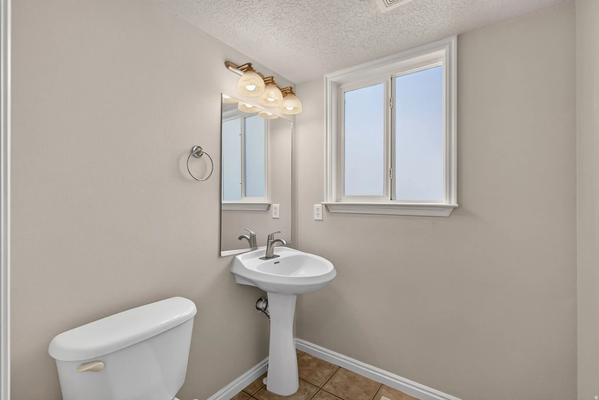 Pedestal sink with chrome faucet, a rectangular mirror, and a three-light vanity fixture