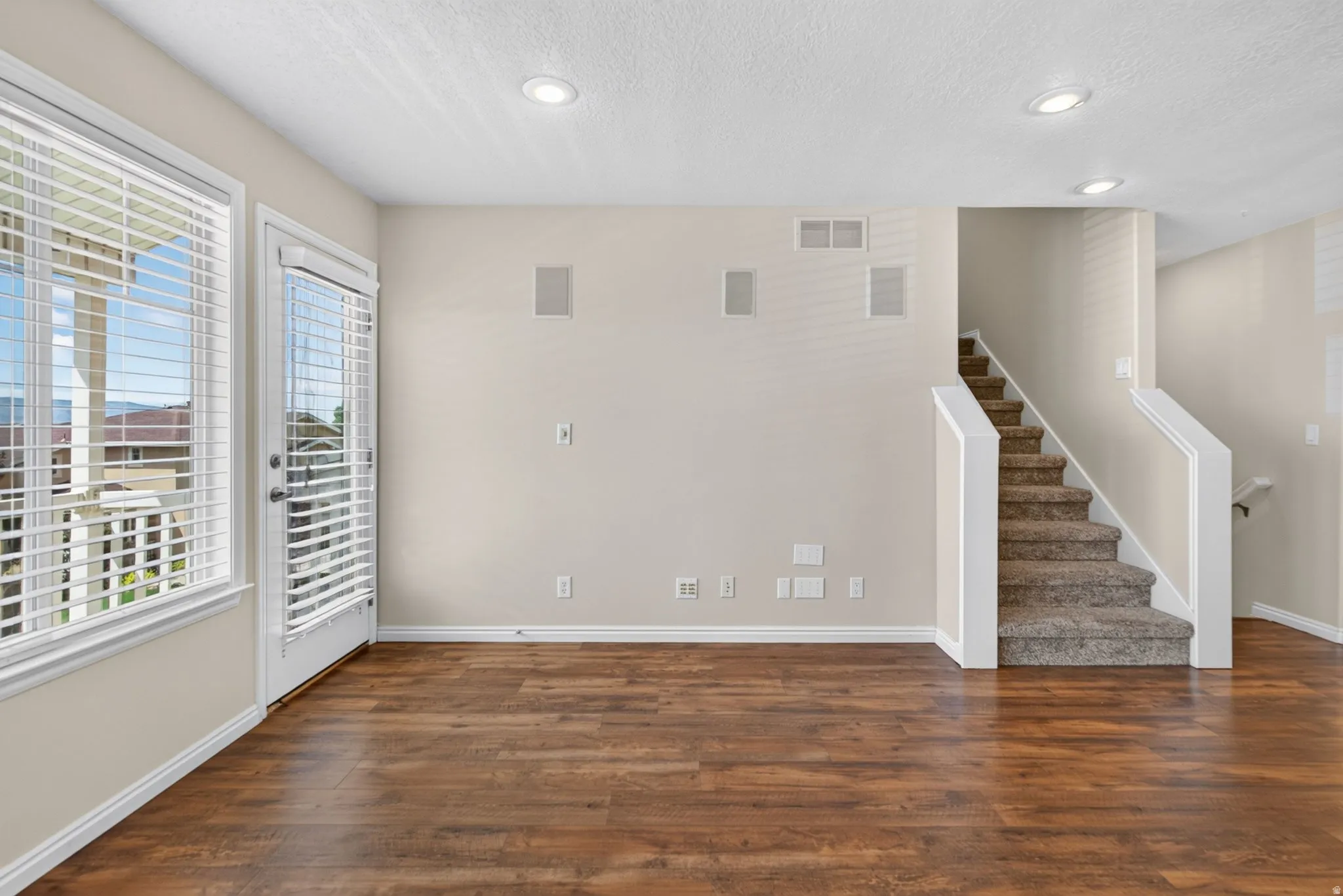 Wood-finish flooring, recessed ceiling lighting, built-in wall speakers, and a staircase with carpeted treads