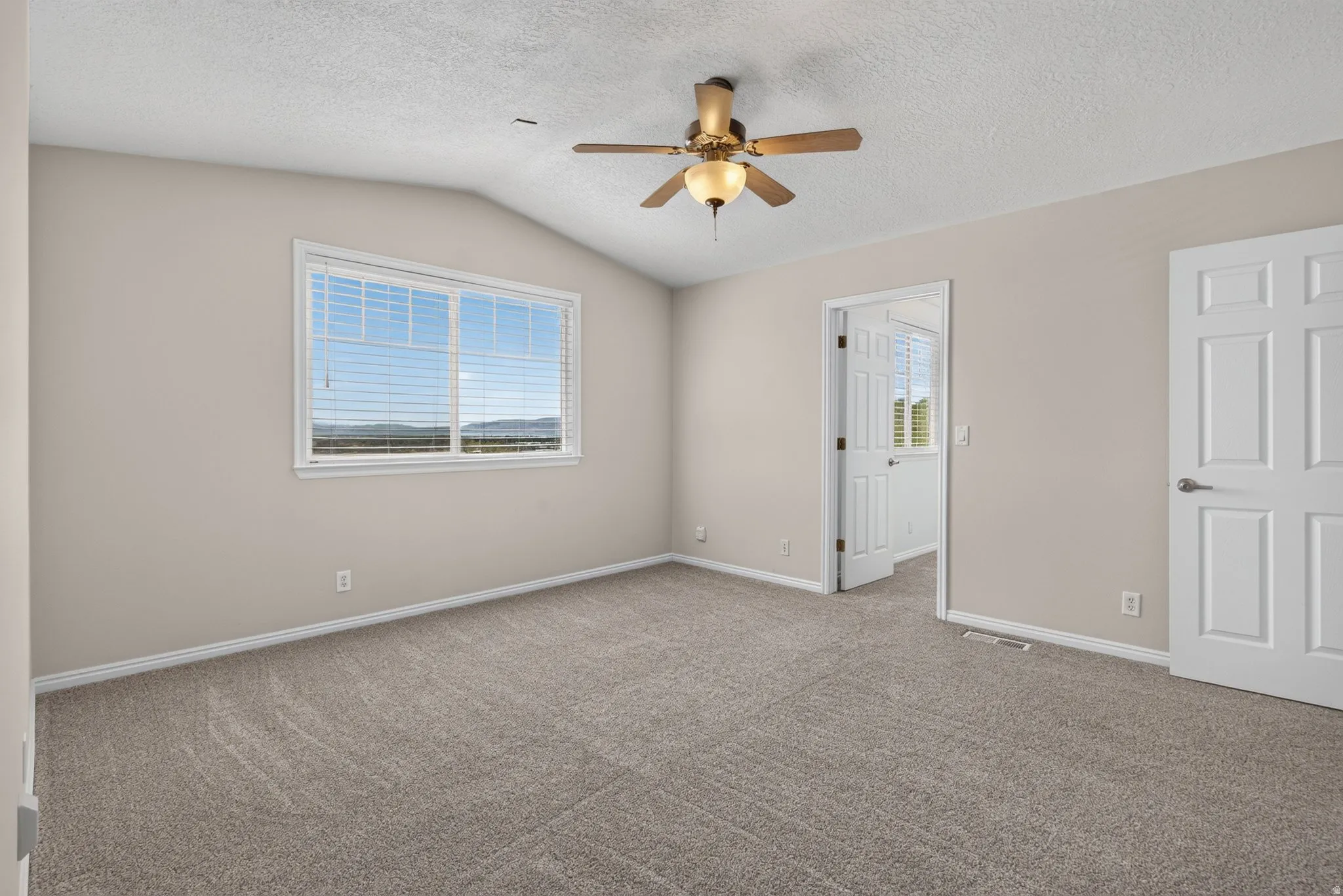 Vaulted ceiling, ceiling fan with integrated lighting, neutral wall paint, carpeted flooring, and a window with blinds