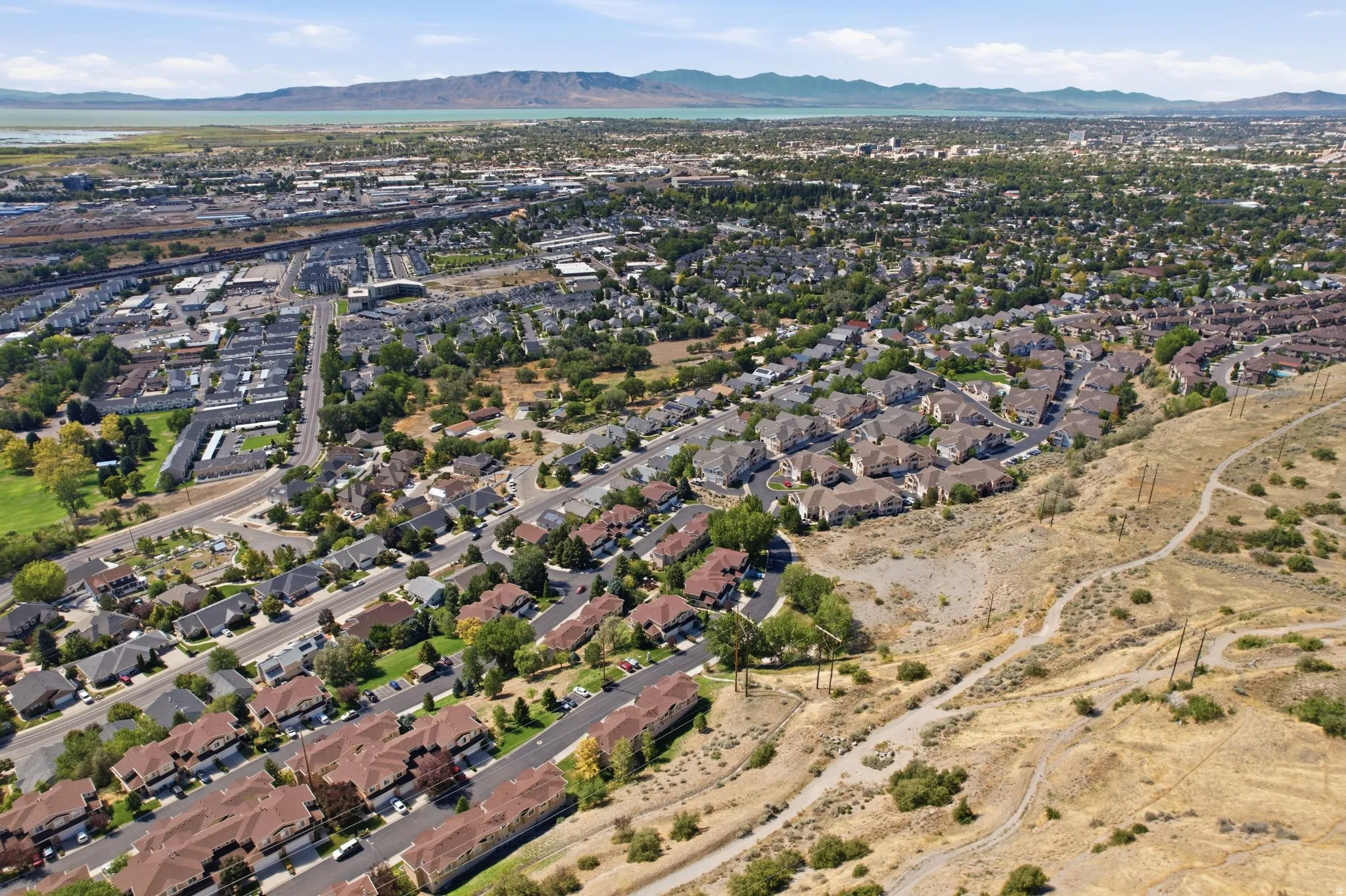 Expansive aerial showing a residential area with varied housing types, green spaces, and a distant body of water