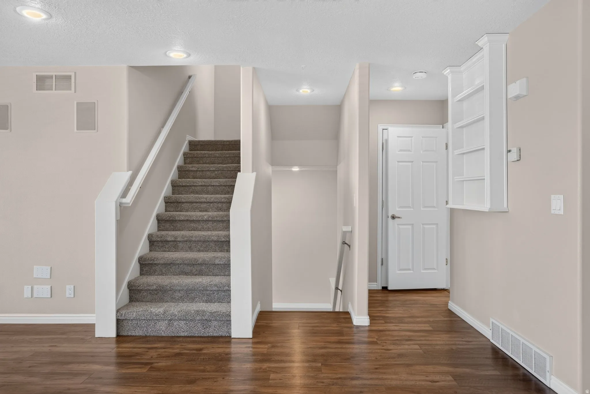 Wood-finish flooring, recessed lighting, carpeted staircase with white railing, built-in shelving, and a six-panel door