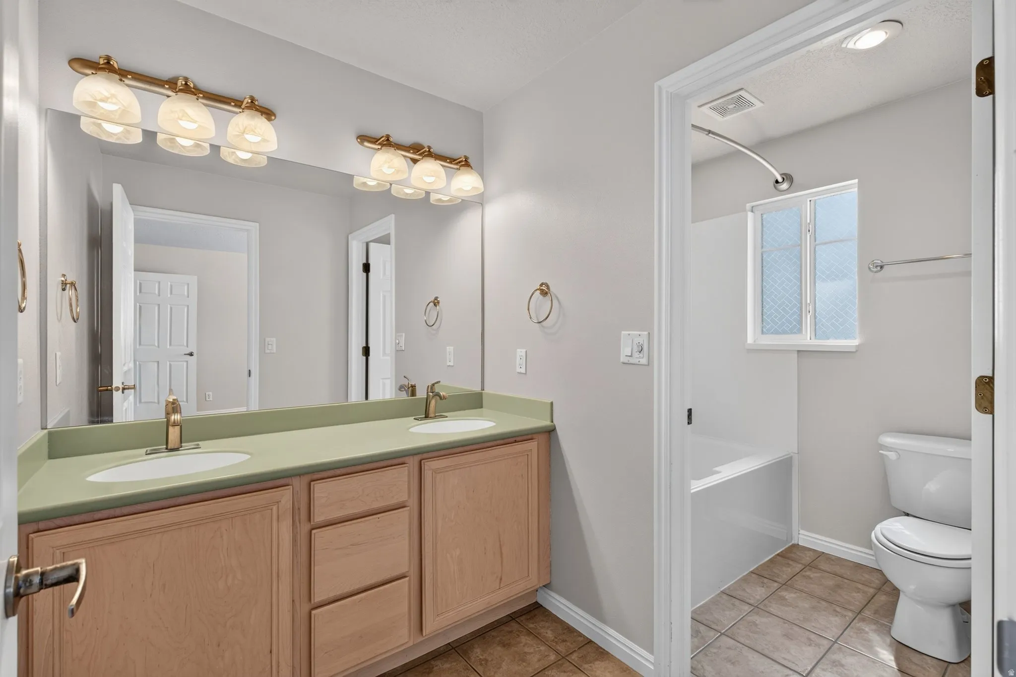 Dual vanity with light wood-finish cabinetry, a single basin tub, and tile flooring