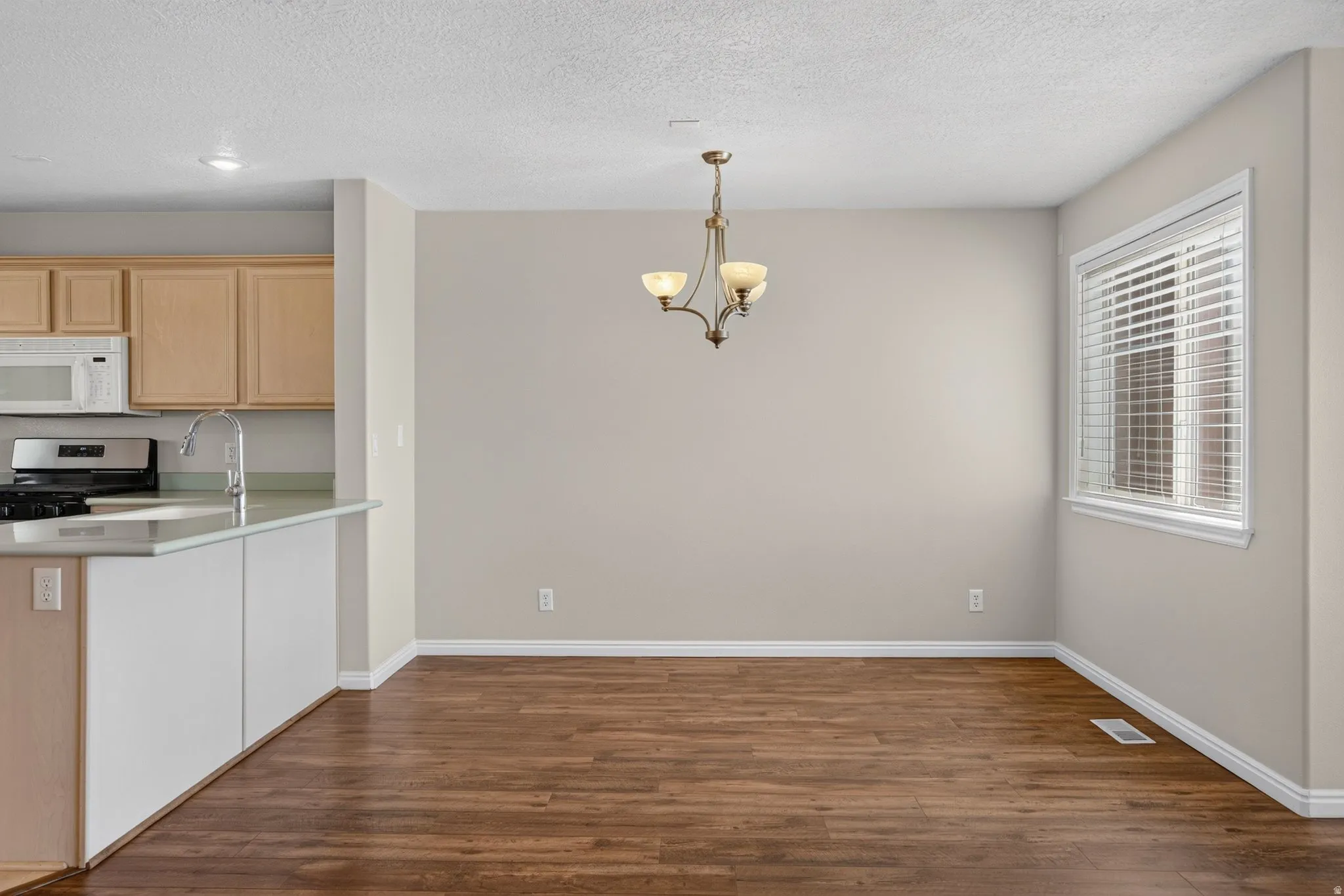 Wood-finish flooring, recessed lighting, bronze-tone chandelier, kitchen peninsula with sink, and a window with blinds