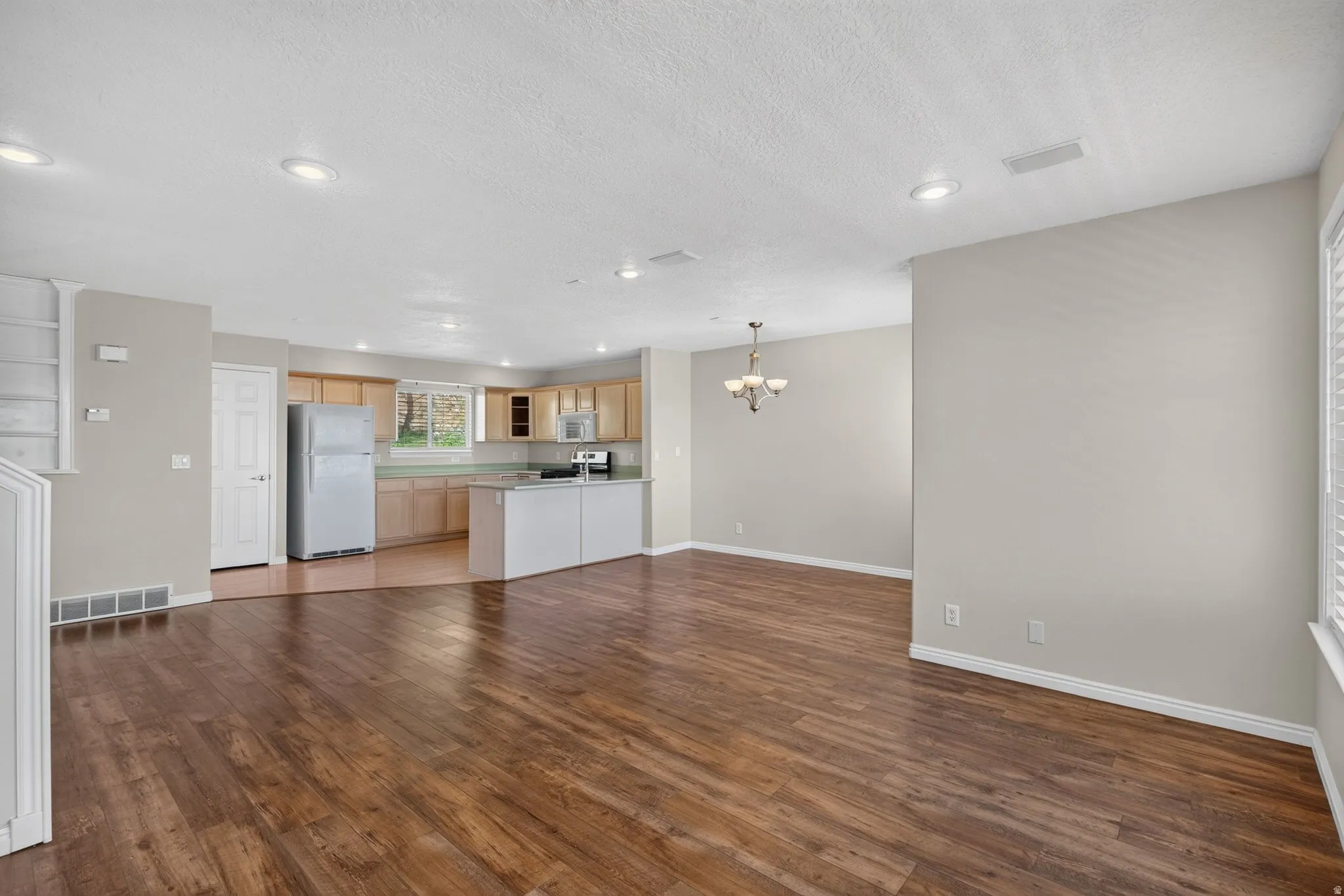 Open-concept living area with wood-finish flooring, recessed lighting, and a kitchen featuring light wood cabinetry and a peninsula