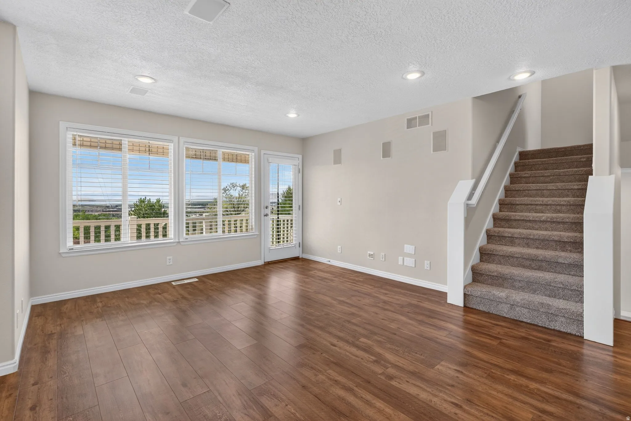 Wood-finish flooring throughout, multiple windows, recessed ceiling lights, and a carpeted staircase