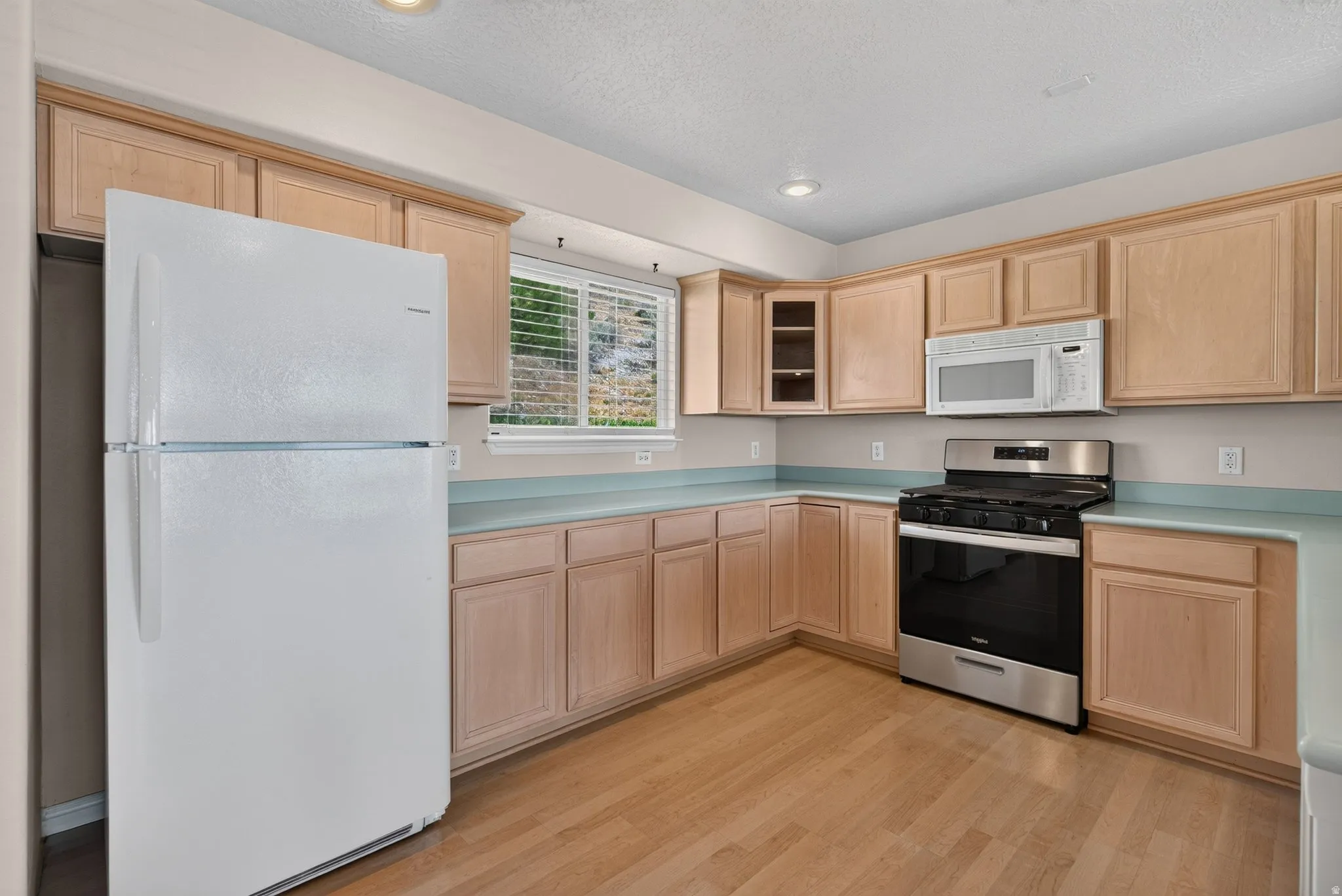 Kitchen featuring light wood cabinetry, light-toned countertops, stainless steel gas range, and wood-finish flooring