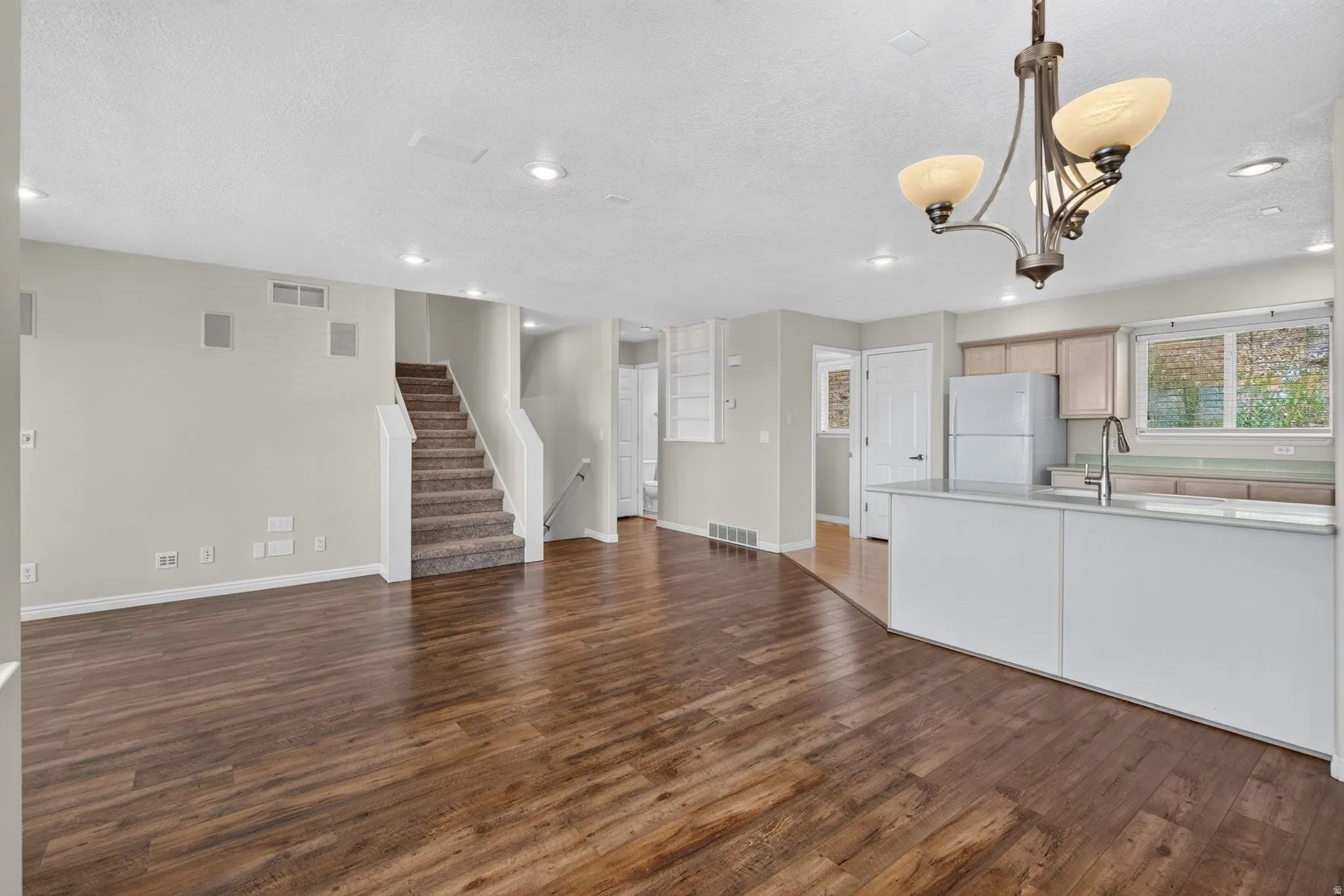 Open-concept living area featuring wood-finish flooring, recessed lighting, and a staircase with carpeted treads