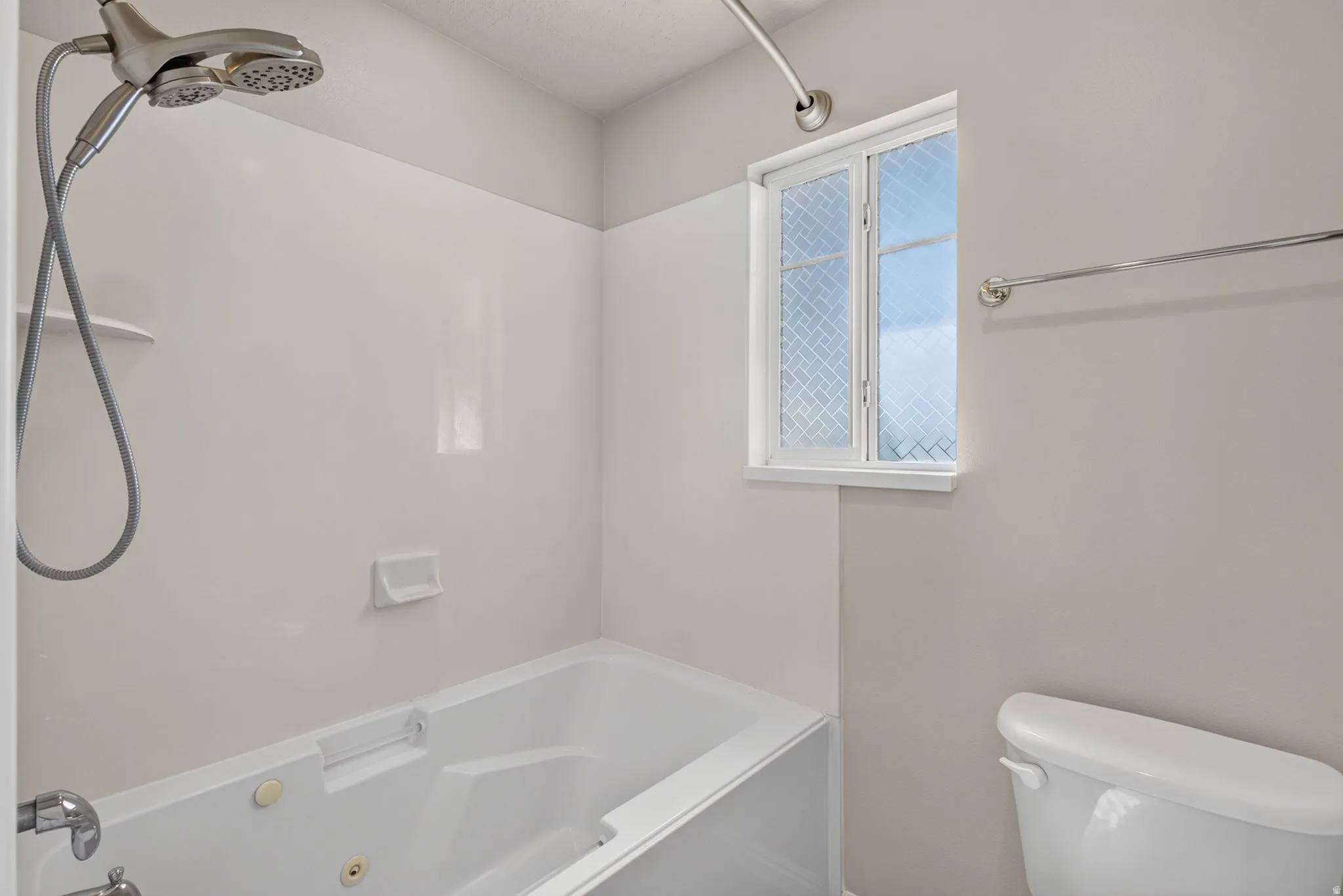 Bathtub with an integrated shower, a dual-head shower fixture, and a textured privacy window