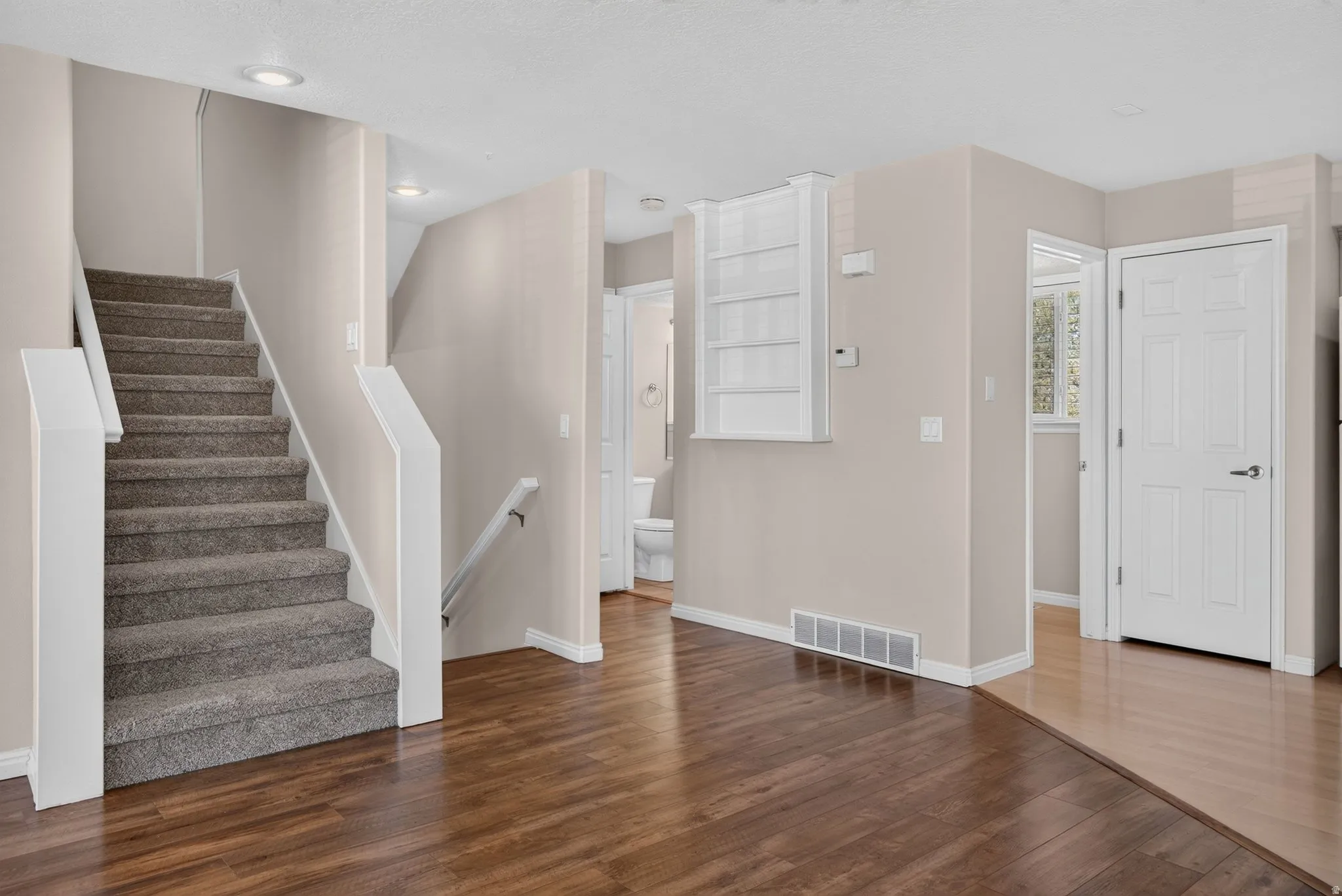Wood-finish flooring, staircase with carpeted treads, recessed lighting, and built-in shelving
