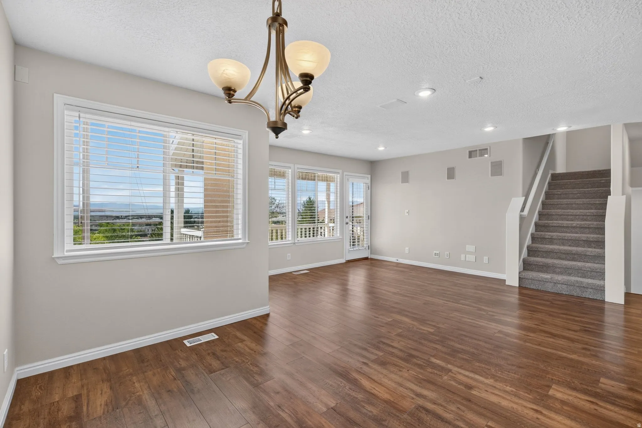Wood-finish flooring, recessed ceiling lighting, a contemporary chandelier, and a carpeted staircase