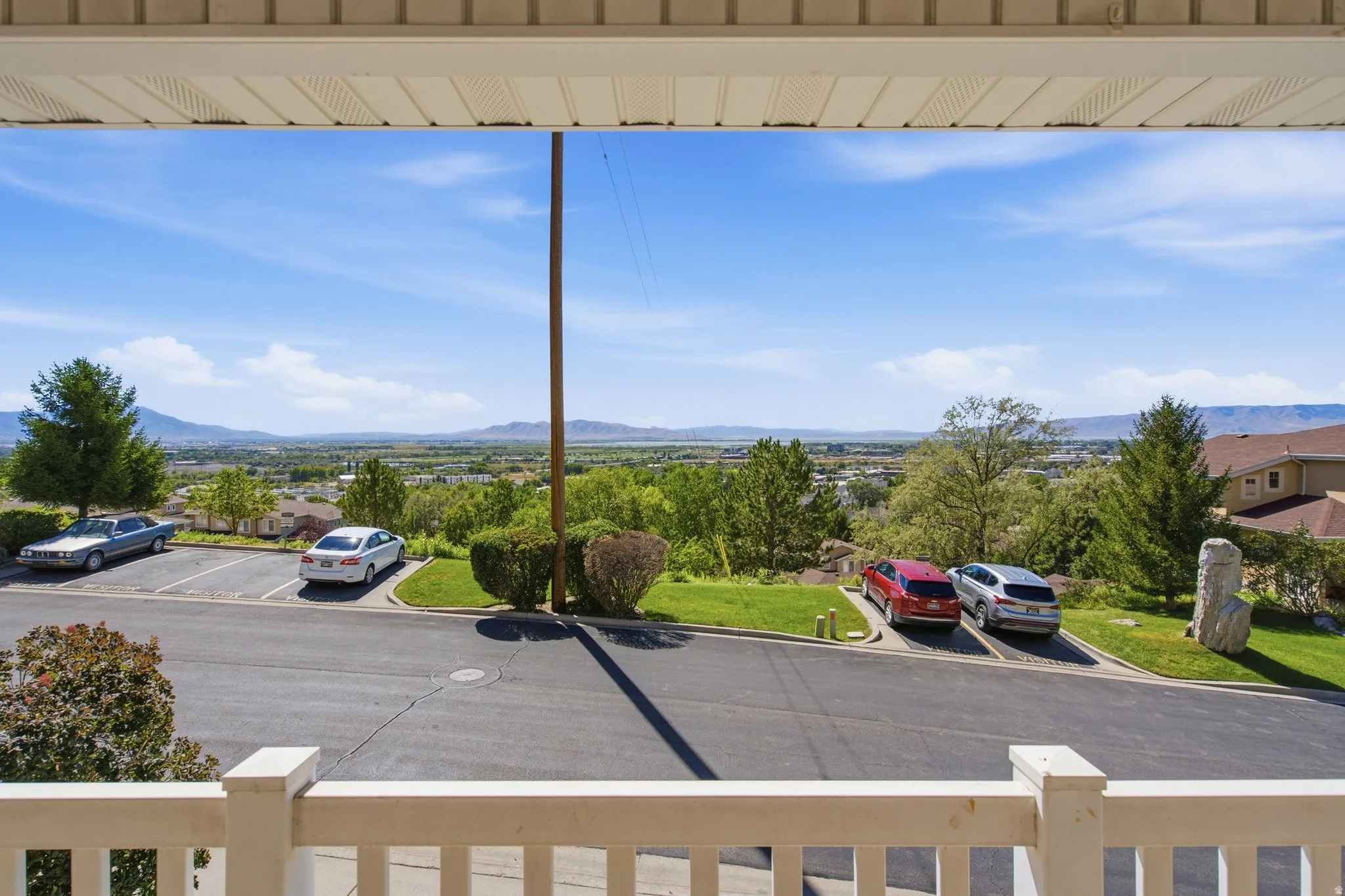 Balcony with white railing and partial soffit, overlooking a paved parking area and distant mountains