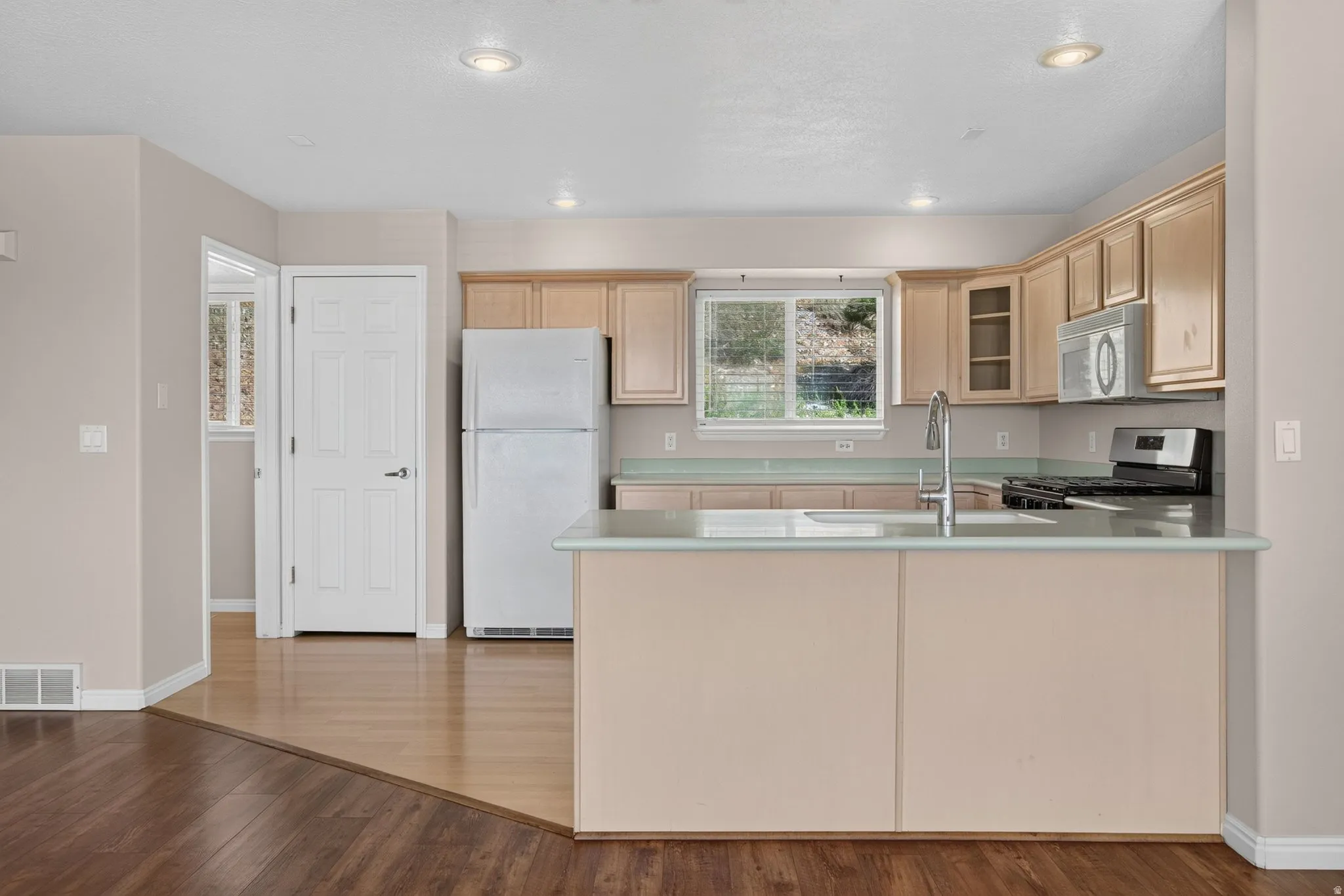Kitchen featuring light wood cabinetry, stainless steel appliances, a kitchen island with sink, and a window with a natural backdrop
