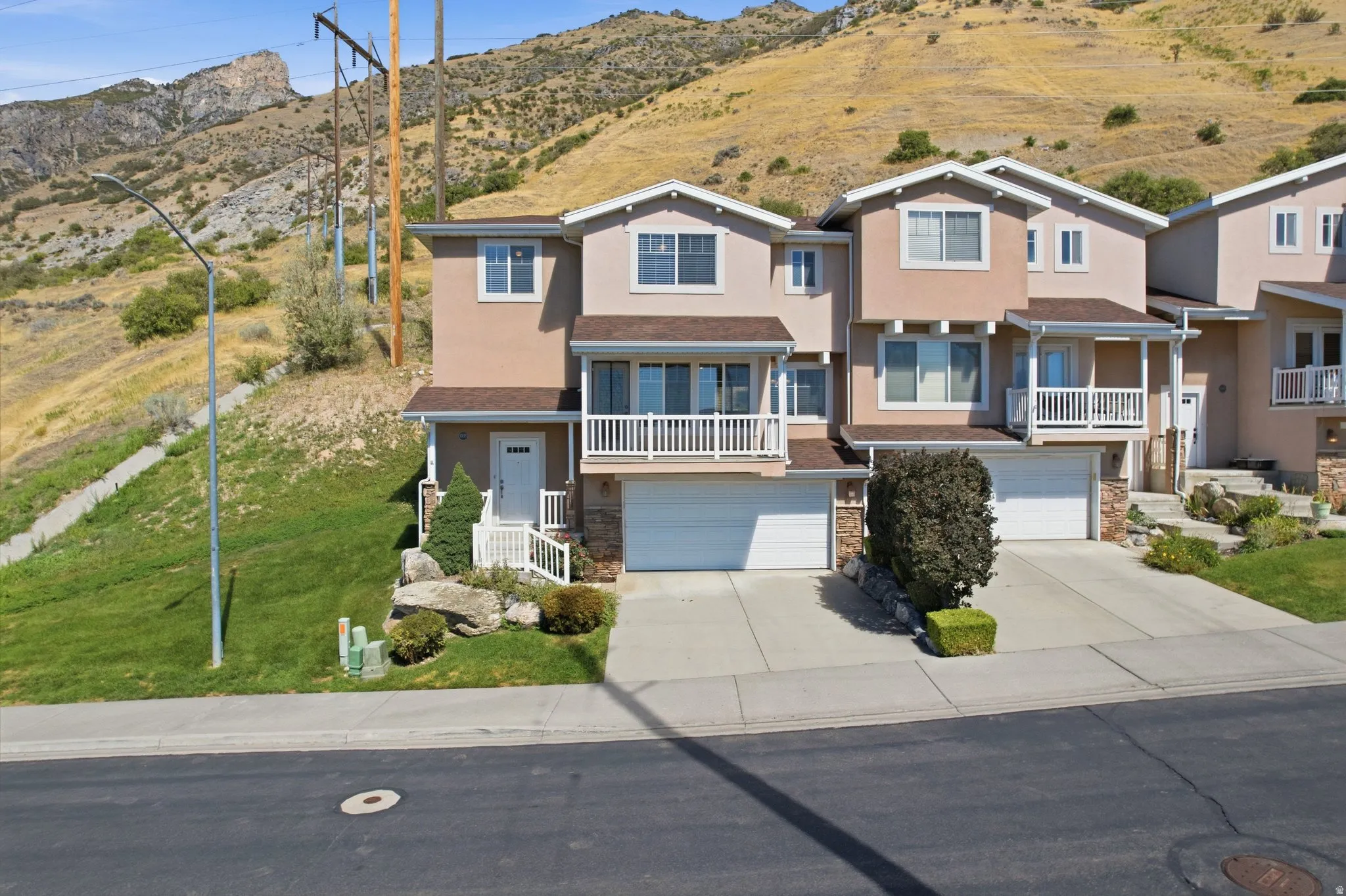 Stucco exterior with stone accents, covered entry, attached garage, white railings, and mature landscaping
