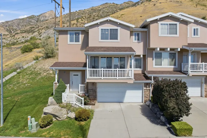Stucco exterior with gabled roof lines, multiple windows, an upper-level balcony, and an attached two-car garage