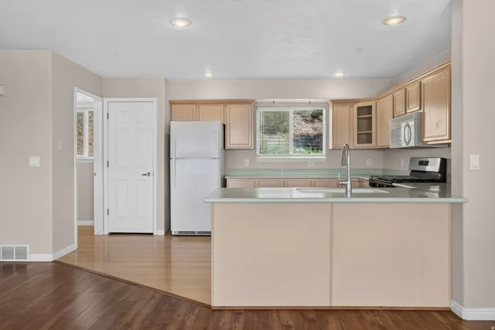 Kitchen featuring light wood cabinetry, stainless steel appliances, a kitchen island with sink, and a window with a natural backdrop