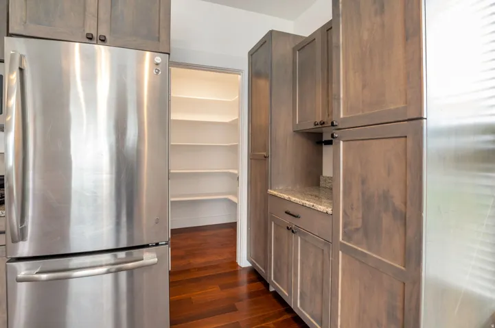 Stainless steel refrigerator, wood-finish flooring, custom wood cabinetry, granite countertop, and walk-in pantry with shelving