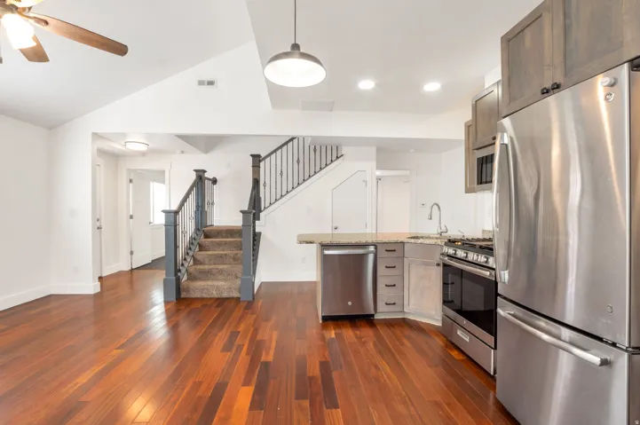 Vaulted ceiling, wood-finish flooring, stainless steel appliances, upper and lower cabinetry, and a carpeted staircase with metal balusters