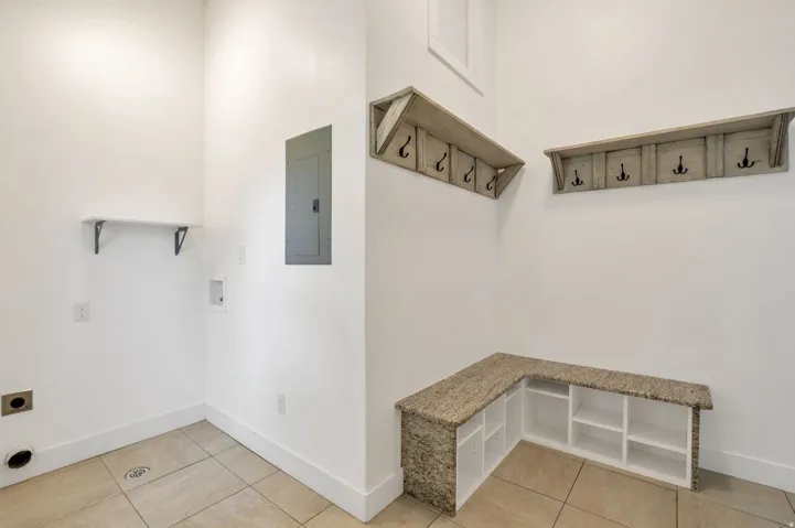 Tile flooring, built-in corner bench with stone-finish top, open shelving, and two wall-mounted coat racks