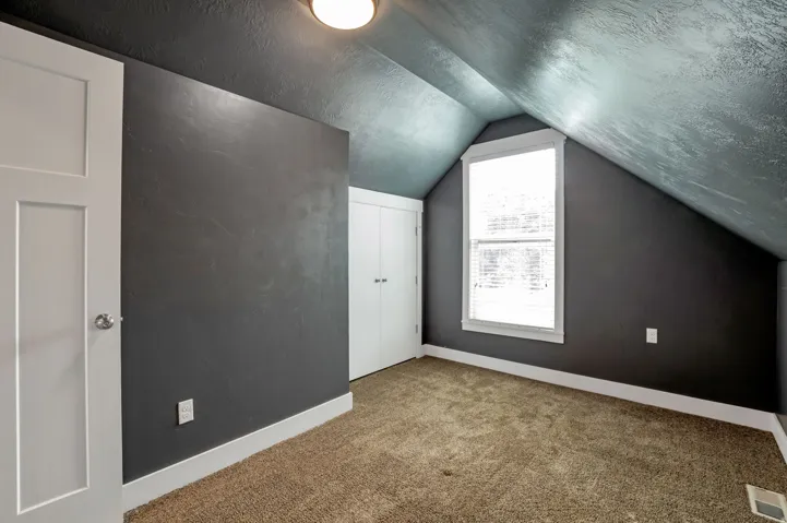 Angled ceiling, carpet flooring, window with blinds, panel doors, and built-in closet