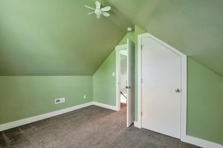 Sloped ceiling room featuring a ceiling fan, plush carpet, and two interior doors