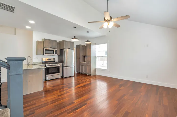 Open-concept living space featuring wood-finish flooring, a vaulted ceiling, and a kitchen with stainless steel appliances, grey cabinetry, and pendant lighting