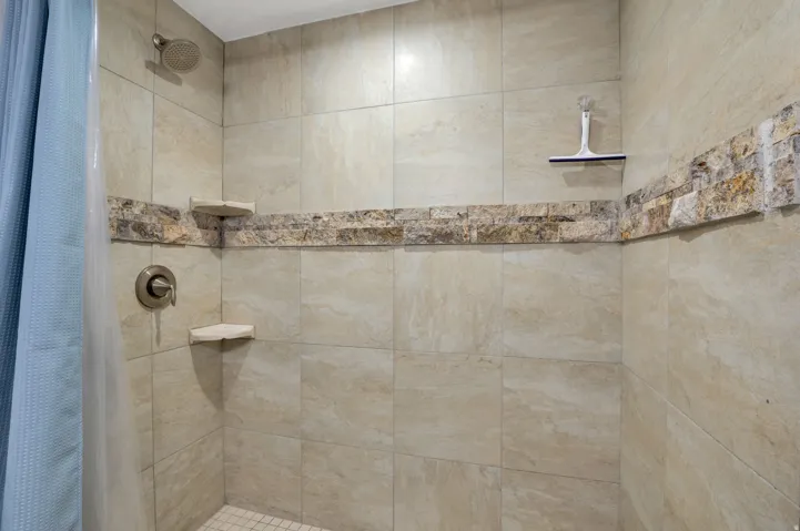 Tiled shower with a decorative stone-finish accent band, built-in corner shelves, and a brushed metal showerhead