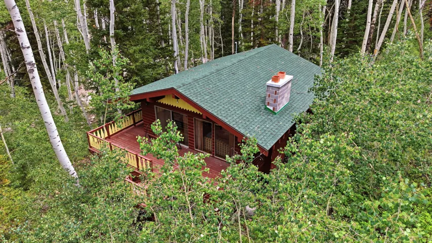 Wood-sided cabin featuring a green shingle roof, a red deck with yellow railing, and a brick chimney