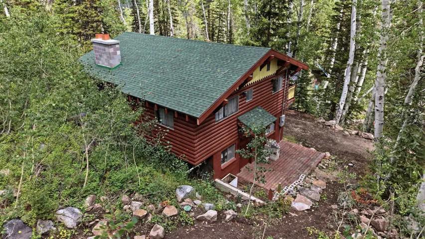 Log cabin exterior with a green shingle roof, stone chimney, and an exterior wood deck