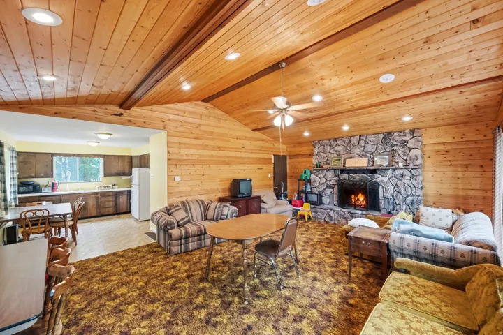 Vaulted wood-paneled ceilings with recessed lighting, stone-clad fireplace, and an open-concept layout to the kitchen