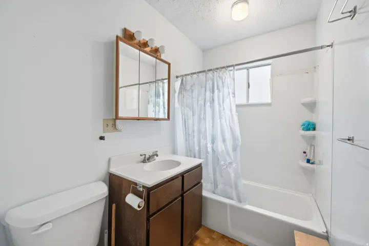 White bathroom featuring a built-in tub with shower, single vanity with integrated sink, wood-finish cabinetry, and a framed medicine cabinet with integrated lighting