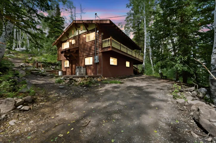 Two-story log cabin exterior with a second-level balcony and a stone foundation