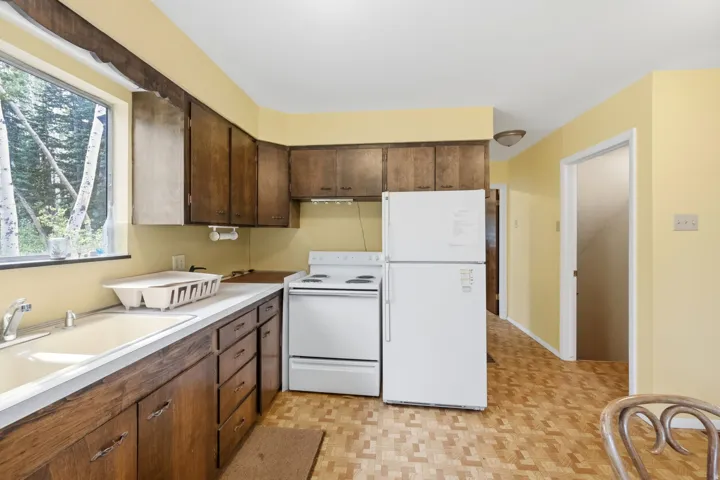 Kitchen featuring wood-finish cabinetry, white countertops, a built-in sink, white appliances, and patterned flooring