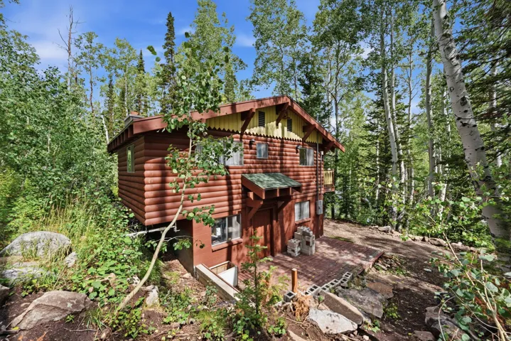Wood-sided cabin exterior with a green shingle roof, surrounded by mature trees and natural landscaping
