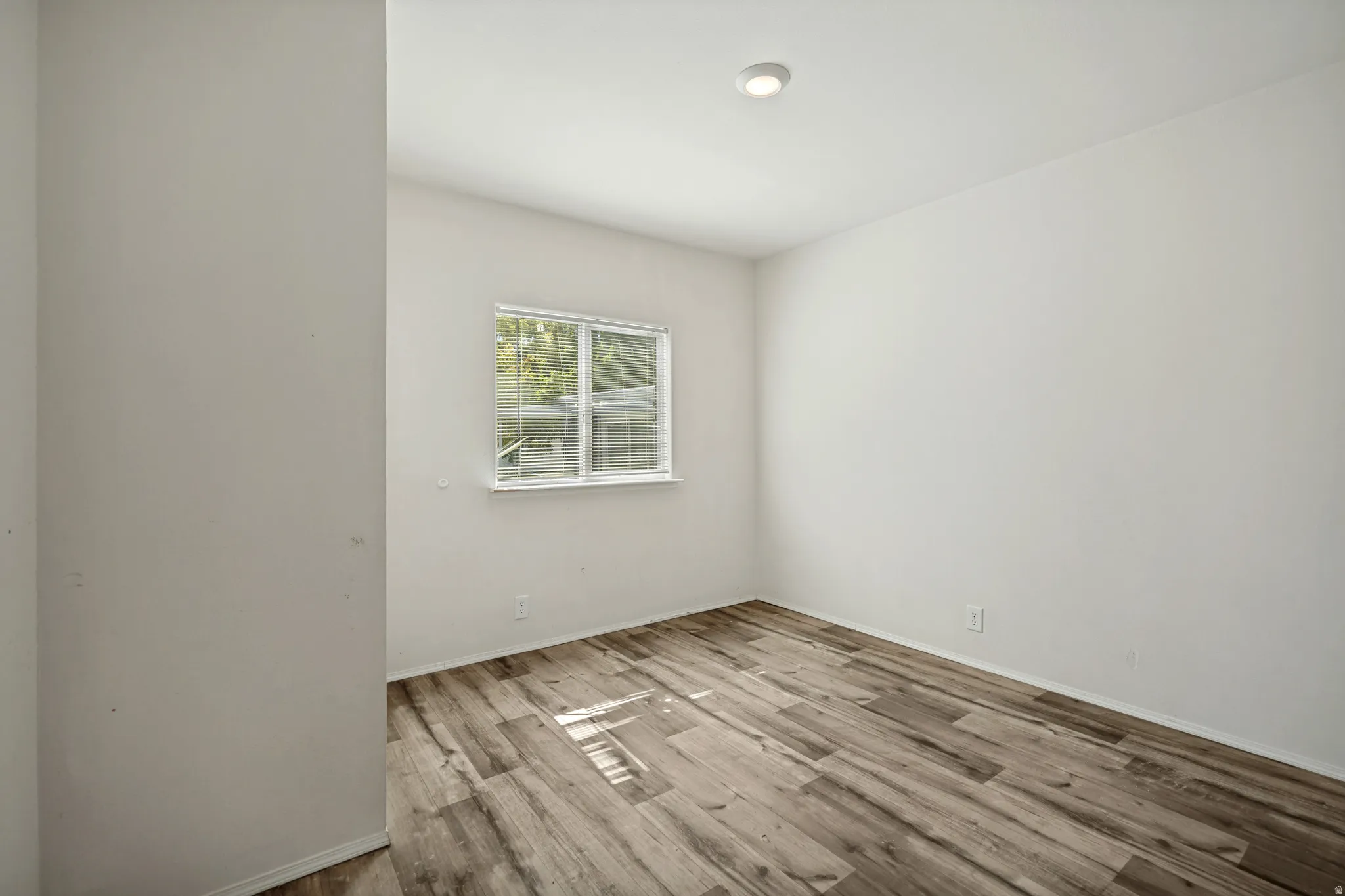 Recessed ceiling light, white painted walls, wood-finish flooring, and a white-framed window