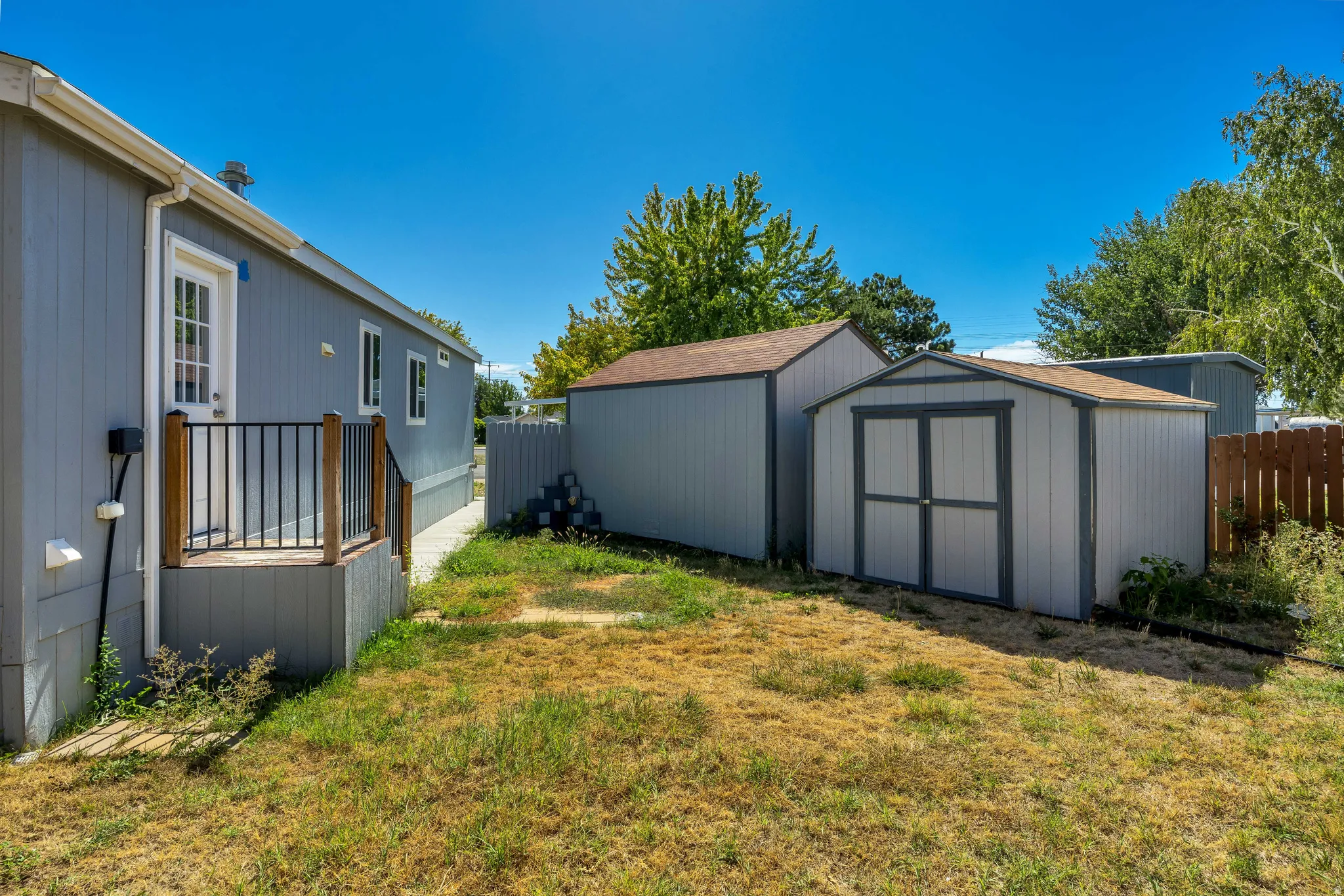 Exterior featuring light blue siding, a deck with black metal railing, two storage sheds, and a wood privacy fence
