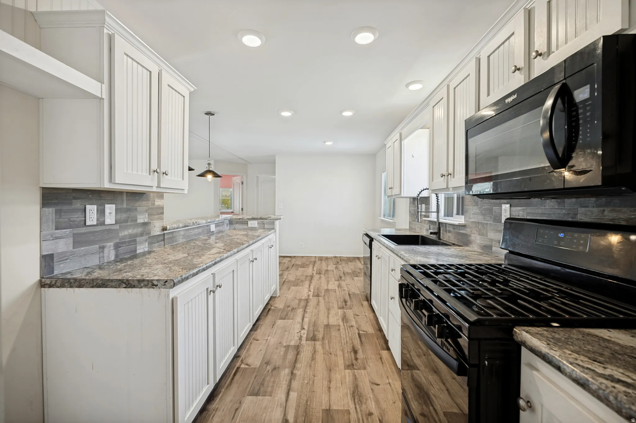 Galley kitchen featuring wood-finish flooring, white cabinetry, integrated black appliances, a tile backsplash, and recessed lighting