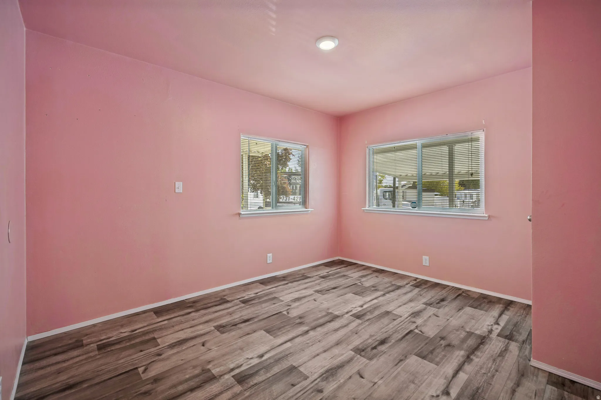 Wood-finish flooring with a matte finish, two windows featuring horizontal blinds, and recessed ceiling lighting