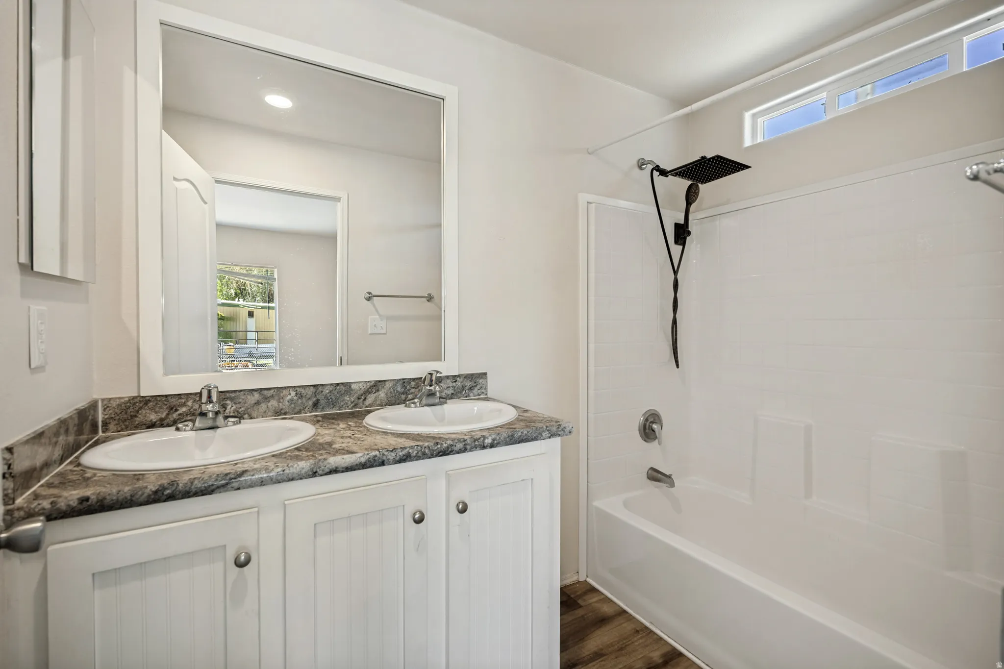 Dual sink vanity with stone-finish countertop, wood-finish flooring, and a shower/tub combination with a rain shower head