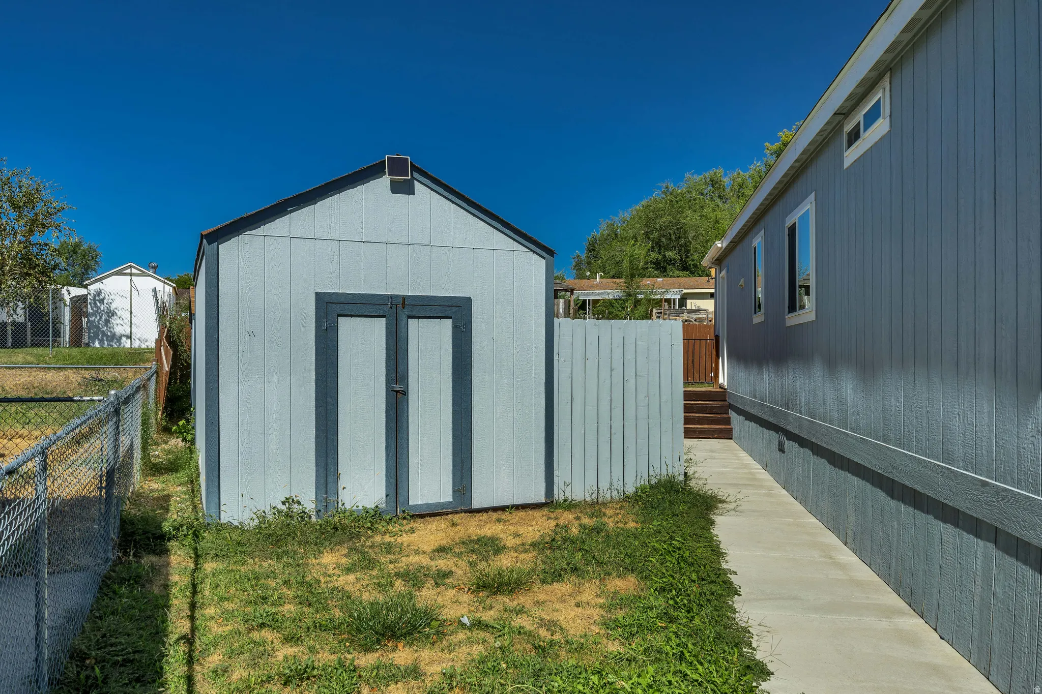 Detached storage shed with gable roof, fenced yard area, and concrete walkway