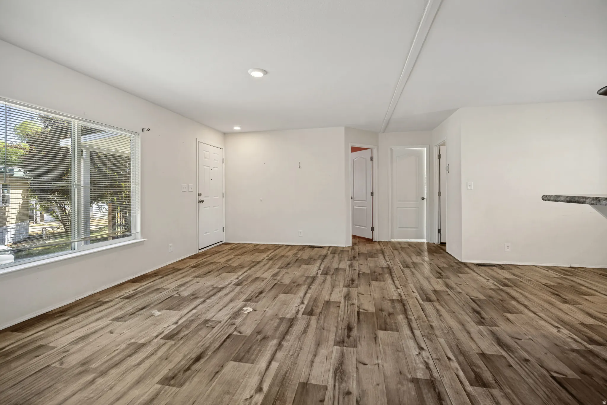 Open-concept living space featuring wood-finish flooring, recessed lighting, and a large front-facing window