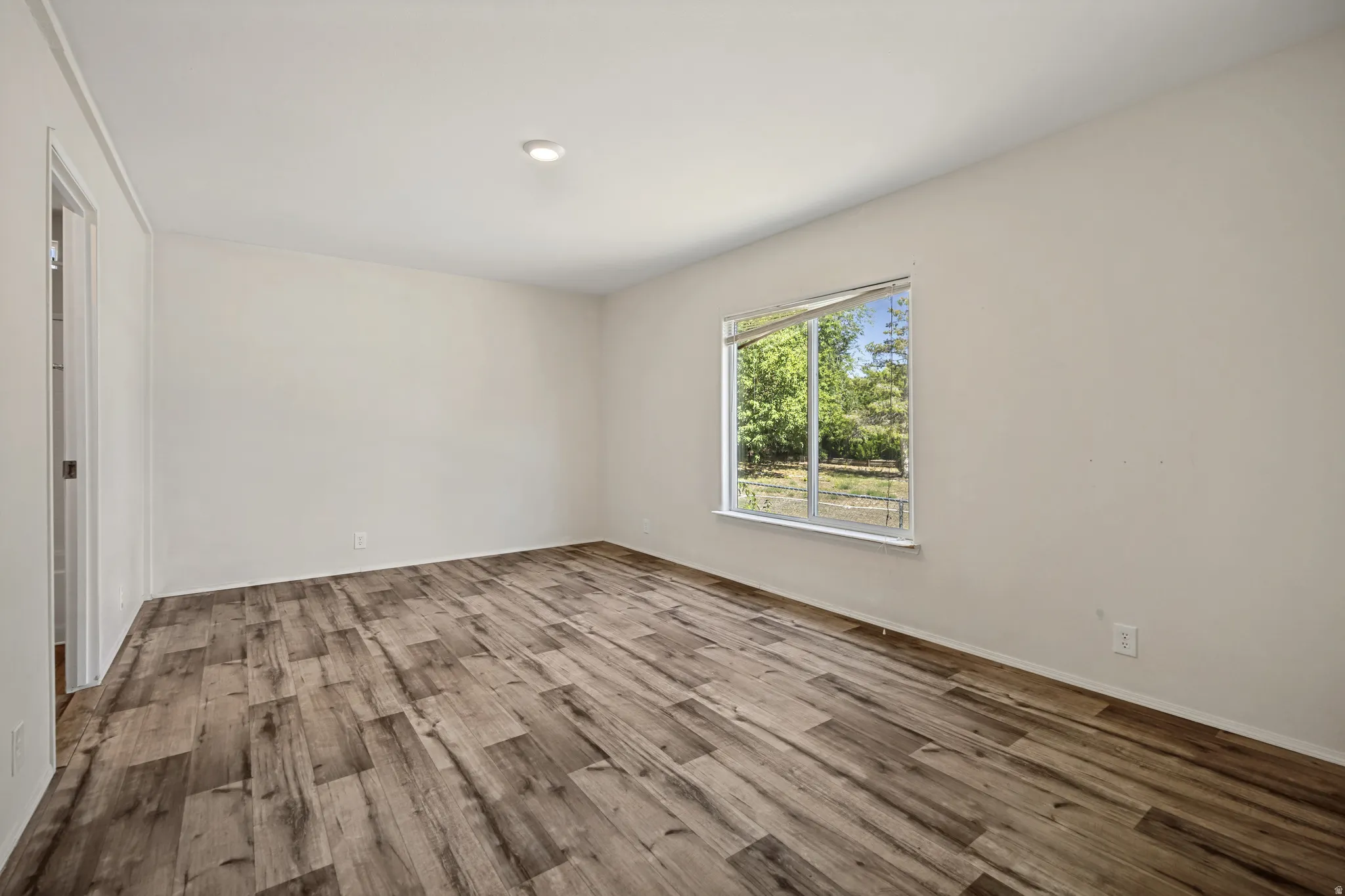 Wood-finish flooring, recessed ceiling light, white walls, and a large window with white trim