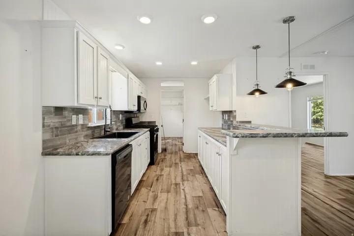 Kitchen featuring white cabinetry, dark stone countertops, wood-finish flooring, recessed lighting, and pendant fixtures
