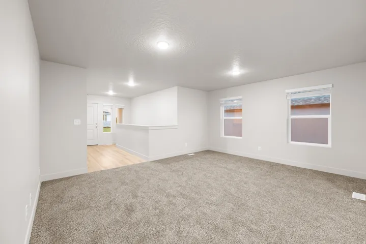 Carpeted living area with two windows, recessed lighting, and a partial wall separating a wood-finish flooring area